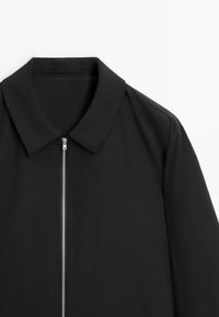 Black collared jacket featuring a zippered front, made from a smooth material with a minimalist design and clean lines.