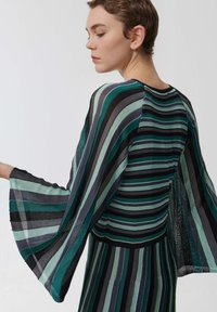 Blouse rayée avec des manches en forme de cloche ; les couleurs comprennent différentes nuances de bleu-vert, noir et gris ; tissu léger avec une finition texturée.