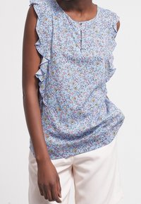 Blouse fleurie bleu clair à manches volantées, dotée de petits boutons au niveau de l'encolure et d'une coupe décontractée. Le motif comprend des fleurs multicolores.