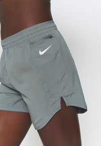 Pantalones cortos deportivos grises con una textura suave, que cuentan con un bolsillo con cremallera lateral y el logo de Nike en blanco. Los bordes deshilachados ofrecen ventilación.
