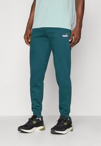 Joggers de un verde azulado oscuro con piernas cónicas, que presentan una cinturilla elástica, una textura sutil y un pequeño logo de Puma en blanco en el muslo izquierdo.