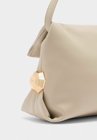 Borsa in pelle beige con una finitura testurizzata, caratterizzata da un accento geometrico dorato sul lato. Il design presenta una silhouette morbida e strutturata.