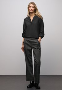 Blusa nera a maniche lunghe con scollo a V e dettaglio di bottoni, abbinata a pantaloni grigi a quadri con tasche laterali e vestibilità comoda. Stivaletti neri alla caviglia.