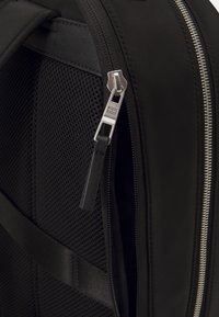 Zaino nero con pannello in rete testurizzata, zip argentata e accenti in tessuto liscio. Dotato di spallacci regolabili e un design elegante.