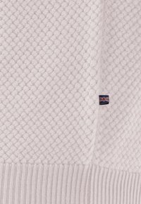 Weißer Strickstoff mit einem kleinen aufgenähten Etikett, das die Flagge des Vereinigten Königreichs in der Nähe einer Naht zeigt.