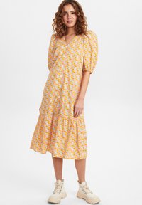 Vestido midi floral em tons de laranja e amarelo com mangas bufantes, decote em V, frente com botões e barra em camadas. Usado com botas bege com atacadores.