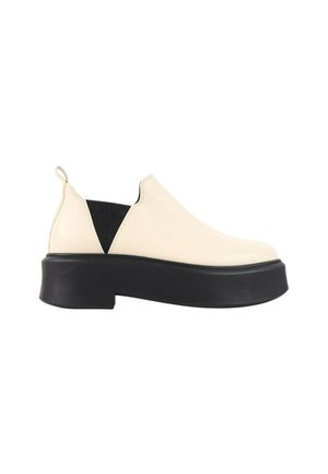 Crèmekleurige slip-on schoen met zwarte elastische zijpanelen en dikke zwarte plateauzool, gezien vanaf de buitenkant.