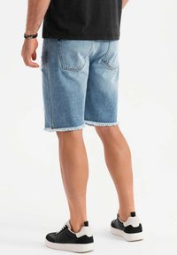 Shorts de denim en azul claro con dobladillos deshilachados, con bolsillos traseros. Combinados con zapatillas negras y blancas.