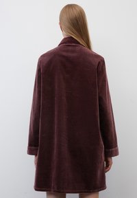 Samettitakki syvän burgundin värissä, jossa on kaulus, pitkät hihat ja käännetyt hihansuut. Tekstuuri on ribatoitu, suora leikkaus, eikä näkyviä sulkijoita.