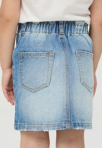 Spódnica dżinsowa w jasnoniebieskim kolorze, z elastycznym paskiem w talii, dwoma tylnymi kieszeniami i surowym dołem. Oferuje casualowy design i trwałą teksturę.