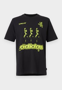 Melna kokvilnas T-kreklu ar spilgti zaļu grafisko dizainu, kurā attēlotas trīs figūras un apakšā ir teksts "adidas". Ar apaļu kakla izgriezumu.