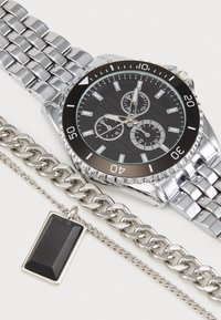 Silver metal watch with a black face, three subdials, and a linked bracelet. Accompanied by a silver chain and a rectangular black pendant.