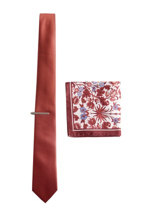 Rote strukturierte Krawatte mit silbernem Krawattenclip neben einem gefalteten weißen Einstecktuch mit rot-blauem Blumenmuster.
