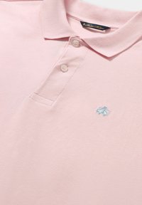 Světle růžové polo tričko vyrobené z texturované tkaniny, s tříknoflíkovou légou a malým modrým vyšitým logem na hrudi.