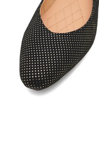 Černá plochá bota s kulatou špičkou, pokrytá vzorem malých odrazivých teček, a s prošívaným béžovým vnitřním podšíváním.