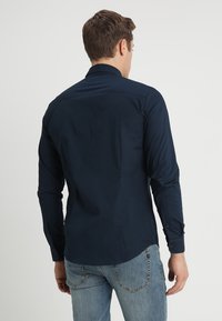 Marineblaue Langarmbluse mit Knopfmanschetten, einem klassischen Kragen und einer glatten Stoffstruktur, kombiniert mit hellblauen Jeans.