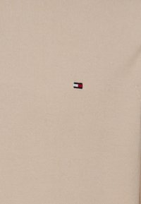 T-shirt in cotone beige con una vestibilità slim, caratterizzato da un piccolo logo ricamato in rosso, bianco e blu sull'area sinistra del petto.