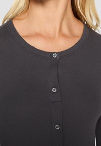 Mörkgrå, ribbad stickad cardigan med rund halsringning och treknappslås. Har subtila fransar vid kragen och en jämn textur.