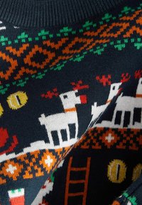 Tissu en maille foncée avec un motif festif représentant des rennes blancs au nez rouge, des formes géométriques vertes et orange, et des dessins circulaires jaunes.