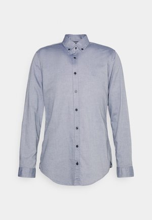 Lyseblå langærmet skjorte med knapper og button-down krave samt mørke knapper, vist mod en ensfarvet lys baggrund.