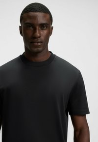 Schwarzes Kurzarm-T-Shirt mit strukturiertem Finish und Rundhalsausschnitt. Der Stoff hat eine glatte Optik und minimale Nähdetails.
