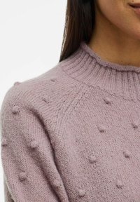 Jasnoróżowy sweter dziany z teksturowanym wzorem, który zawiera małe wypukłe kropki oraz ściągaczowy dekolt. Miękki materiał i luźny krój.