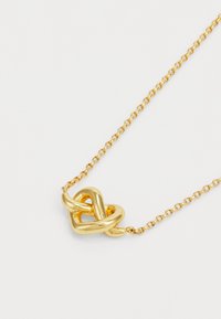 Colar de ouro com um pingente em forma de nó torcido em corrente delicada, destacando a textura metálica polida e formas suaves e arredondadas.