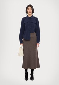Navy button-up shirt with flap pockets, paired with a textured brown ribbed midi skirt. Model holds a small cream handbag and wears black ankle boots.