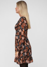 Langdurige mouw bloemdress in donkerbruin met oranje en groene bladerenpatronen, gesmockte zoom en aansluitende taille. Semi-doorschijnende stofstructuur.