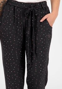 Černé kalhoty s volným střihem, které mají pás se stahovací šňůrkou. Ozdobené malými, vícebarevnými vzory listů a bočními kapsami.