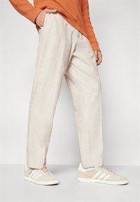 Lysebeige linnedragt med en afslappet pasform, featuring sidelommer, parret med beige sneakers med hvide striber og branding.