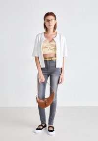 White cropped cardigan, gold satin top, gray skinny jeans, yellow belt, brown crocodile-textured handbag, black and white platform shoes.