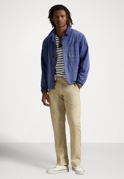 Ikdienišķs apģērbs ar zilām pogām aiztaisāmu jaku, svītrainu kreklu, haki krāsas biksēm un baltām sporta kurpēm. Jakai ir krūšu kabata un brīvs piegriezums.