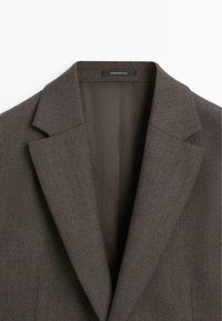 Blazer marrone su misura con colletto a lancia, texture liscia e due tasche frontali; realizzato in tessuto strutturato. L'etichetta riporta "Made in Portugal."