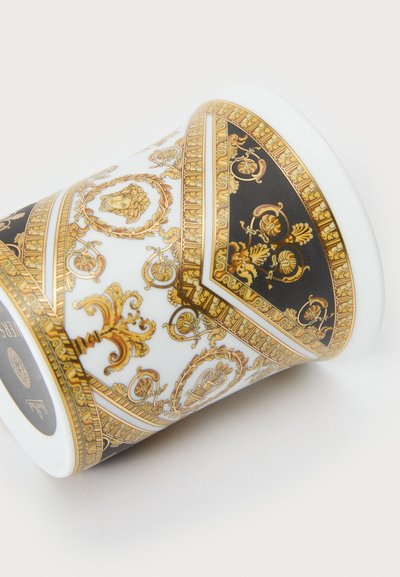 Taza de porcelana con intrincados patrones dorados y negros, que presenta un diseño clásico con detalles ornamentales y un acabado liso y brillante.