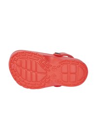 Red rubber sandal sole with textured grip patterns, ventilation holes, and a strap with a black button closure. Smooth surface finish.
