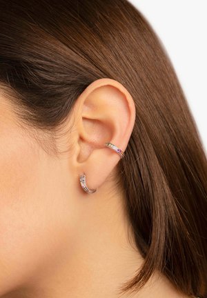 Silberne Creolen mit geschwungenem Design, die an der Vorderseite mit mehrfarbigen Edelsteinen verziert sind, getragen in einem gepiercten Ohr.