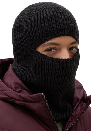 Czarna dziana kominiarka o ribbowym wzorze, zakrywająca głowę i szyję. Noszona z burgundową kurtką puchową, częściowo widoczną w kadrze.