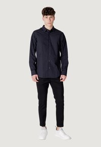 Camicia blu navy con pois bianchi, maniche lunghe, abbinata a pantaloni slim-fit neri e sneakers bianche. Tessuto morbido e vestibilità su misura.