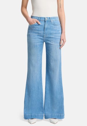 Light blue denim flared jeans with a high waist, front pockets, and a clean hem finish; worn with a fitted white top and white shoes.