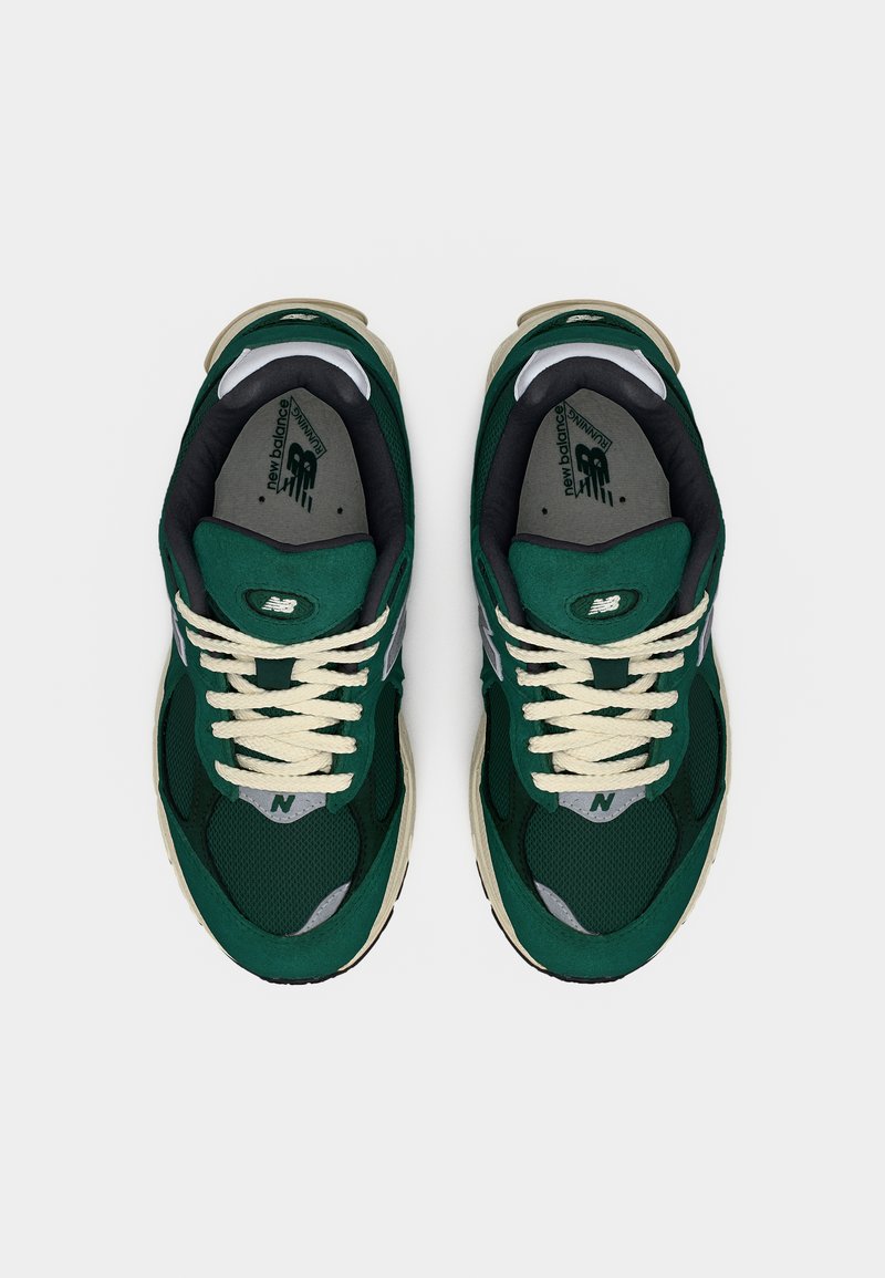 Paire de baskets de course New Balance vert foncé avec lacets beige et doublure intérieure noire, vues de dessus sur un fond blanc.