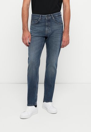 Blauwe denim jeans met een rechte pasvorm, vijf zakken en vervaagde details. G gedragen met witte sneakers en een zwart T-shirt.