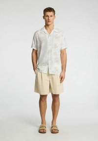Kortærmet skjorte i let stof med et subtilt blomstermønster, parret med beige shorts og brune sandaler. Ren, afslappet pasform.
