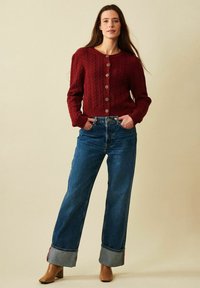 Röd stickad cardigan med strukturerat mönster och fem knappar, i kombination med blå vida jeans med uppvik och beiga klackstövlar.