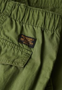 Groene utility shorts met een elastische tailleband, voorzien van een stoffen label in zwart en oranje met de tekst "Superdry" en maatdetails.