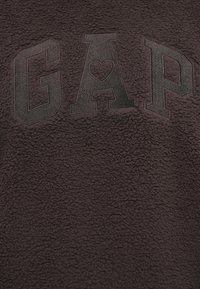 Sudadera de forro polar gris oscuro con un logo en relieve de "GAP" que incluye un corazón en la letra "A". Tejido suave y texturizado con una apariencia acogedora.