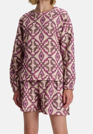Frau trägt ein passendes langärmeliges Oberteil und Shorts mit einem pinken und braunen geometrischen Diamantmuster.