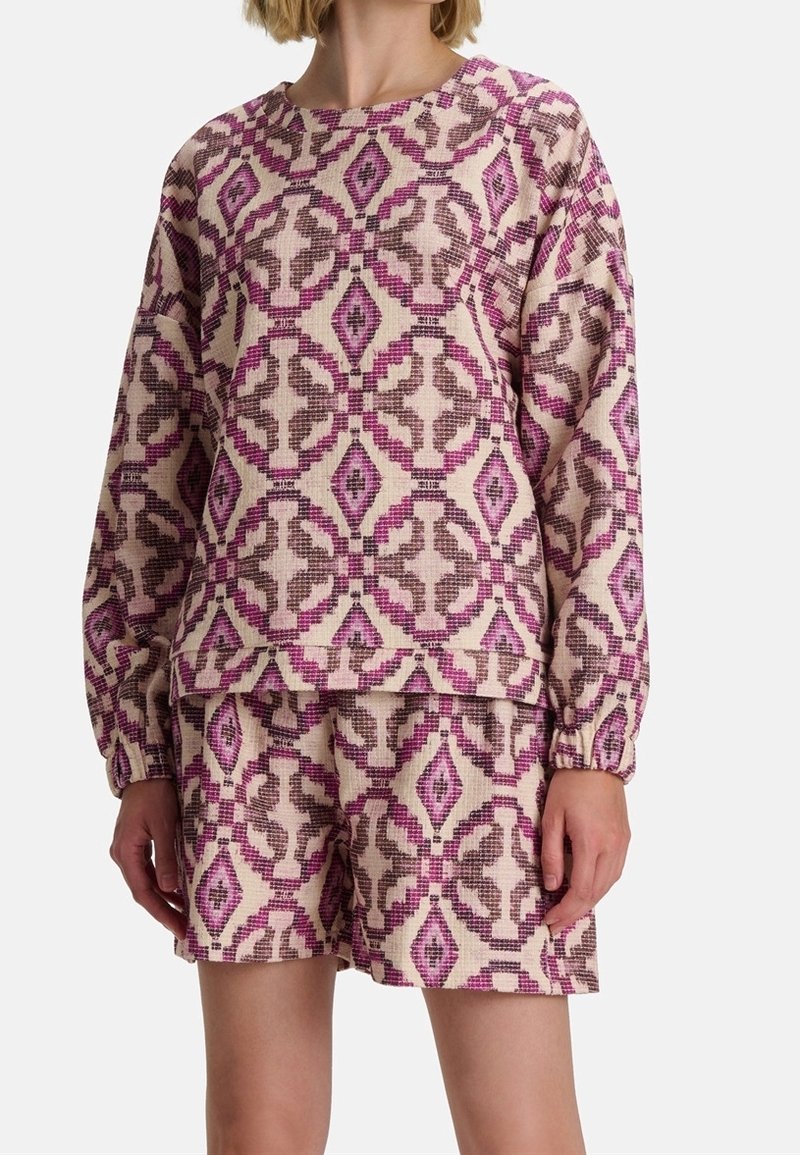 Femme portant un haut à manches longues et un short assortis avec un motif géométrique en losanges rose et marron.
