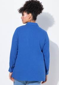 Camicia blu button-up in tessuto texturizzato, con maniche lunghe e colletto classico. Presenta una vestibilità rilassata e un dettaglio sullo yoke posteriore.