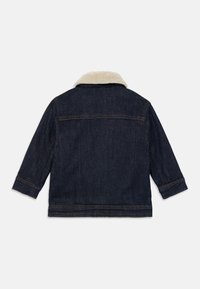 Chaqueta de mezclilla azul oscuro con costuras en color beige y un cuello de sherpa color crema, mostrada desde la parte posterior sobre un fondo blanco.